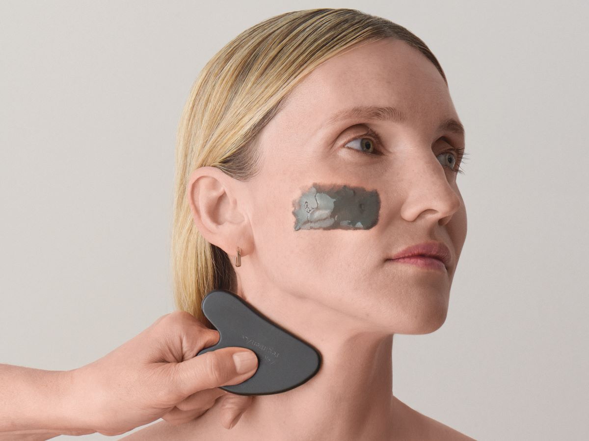 woman using a gua sha and a charcoal mask